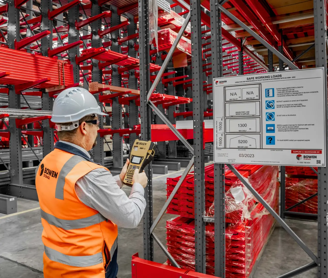 Worker conducting pallet racking safety inspection with scanner in warehouse storage system