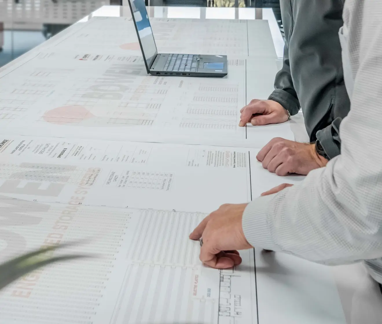 Team reviewing warehouse layout plans and storage design drawings on table with laptop