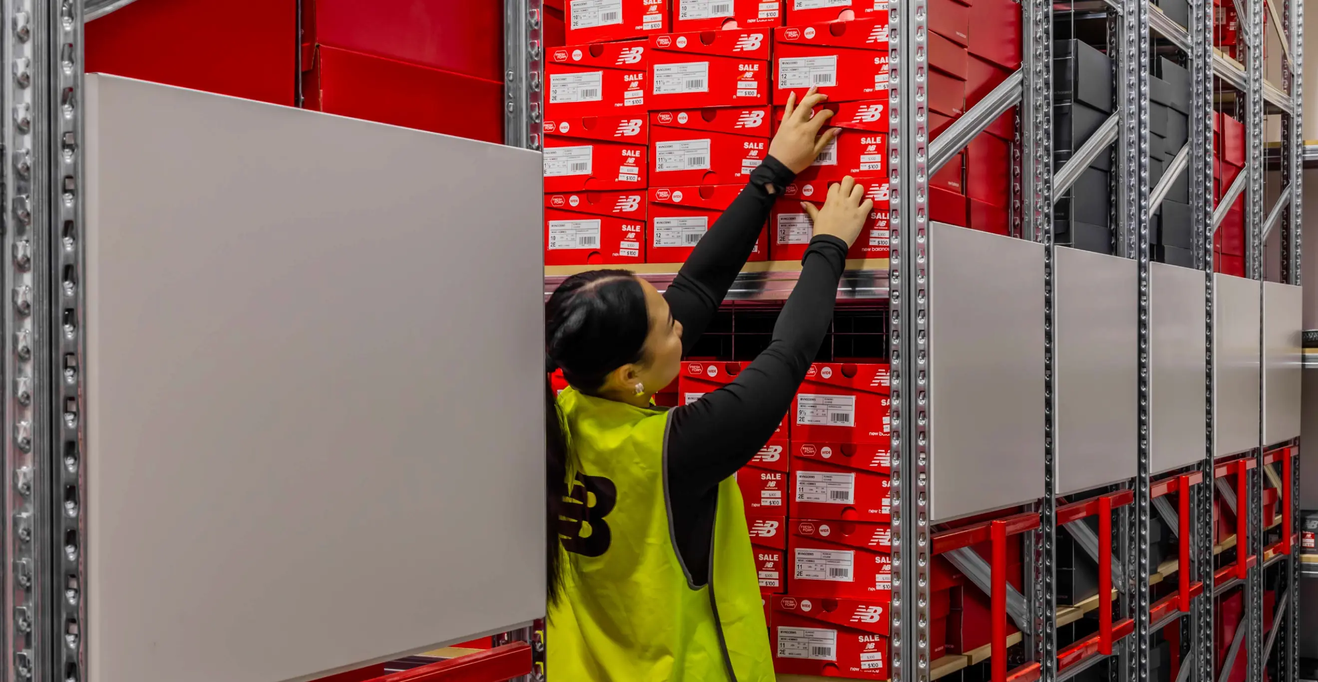 Worker retrieving shoe boxes from high-density compact shelving system in retail stockroom environment