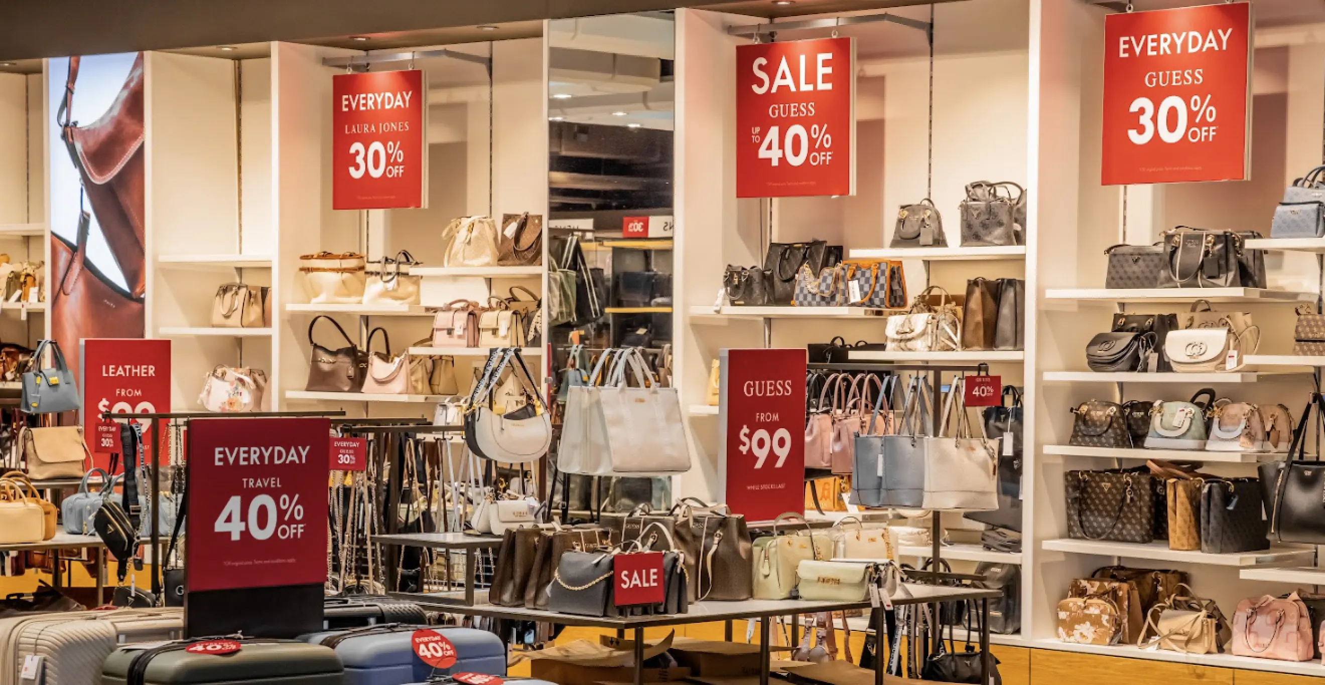 Retail store interior with handbag displays, shelving units, and promotional sale signage
